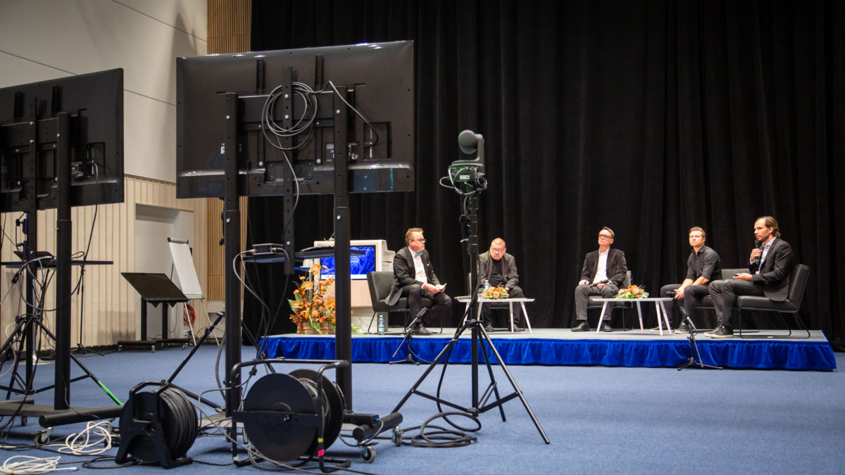 Paneelikeskustelu AI Finland -tapahtumassa. Viisi miestä istuu tuoleilla.